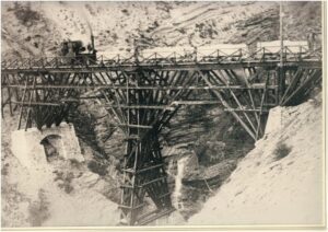 Il trenino con i vagoncini carichi di materiale passa su un ponte di legno – Archivio Centrale Enel di Farneta